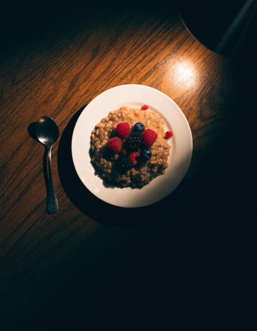 A plain plate of whole grain porridge and berries on a dark table under one warm lamp